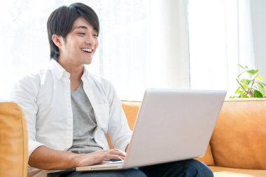 Laptop kullanan mutlu Asyalı genç adam.