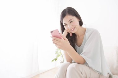 Asyalı kadın evde akıllı telefon kullanıyor.