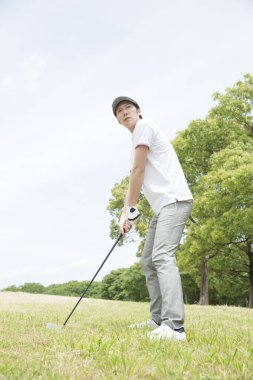 Beyaz gömlekli ve gri pantolonlu bir Asyalı golf oynuyor.