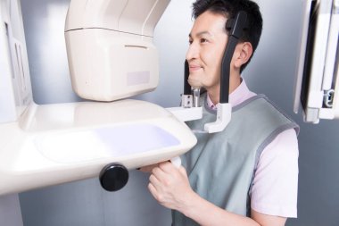 Asyalı adam gülümseyen bir makineye bakıyor, çenesinin 3 boyutlu resmini yapıyor.