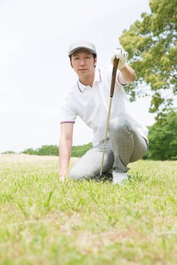 Beyaz gömlekli ve gri pantolonlu bir Asyalı golf oynuyor.