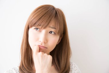 Asyalı genç bir kadın soyutlanmış arka planda hüzünlü bir ifadeyle düşünüyor.