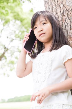 Yaz parkında akıllı telefon kullanan tatlı Japon kız, komik çocuğun gündüz portresi.