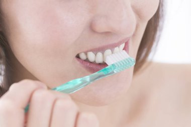 Beyaz arka planda dişlerini fırçalayan güzel bir Japon kadının portresi.