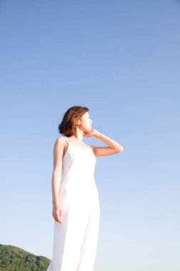 Beyaz elbiseli güzel Asyalı kadının portresi mavi gökyüzü arka planına poz veriyor.