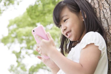 Yaz parkında akıllı telefon kullanan tatlı Japon kız, komik çocuğun gündüz portresi.