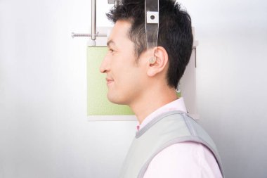 Asyalı adam gülümseyen bir makineye bakıyor, çenesinin 3 boyutlu resmini yapıyor.