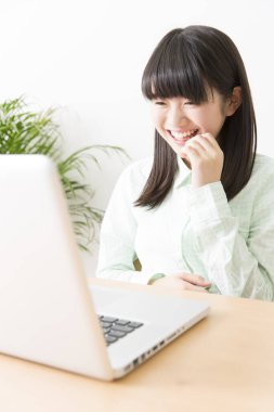 Gülümseyen Japon kız dizüstü bilgisayarla masada oturuyor.