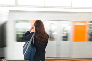 Asyalı kadın öğrenci metro istasyonunda tren bekliyor.