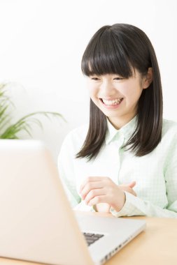 Gülümseyen Japon kız dizüstü bilgisayarla masada oturuyor.