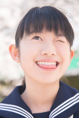 Parkta poz veren güzel Asyalı kız okulunu kapatın. Arka planda çiçek açan ağaçlarla.