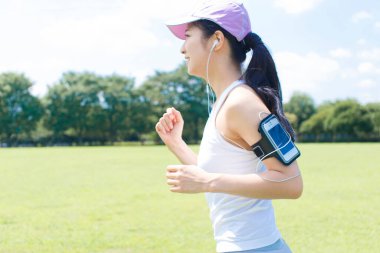 Parkta akıllı telefonlu genç bir kadın koşuyor.