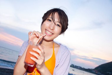 Genç Asyalı kız gün batımında meyve suyu içiyor.