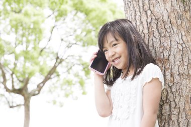 Yaz parkında akıllı telefon kullanan tatlı Japon kız, komik çocuğun gündüz portresi.