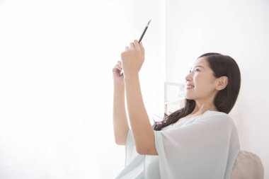 Evde akıllı telefon kullanan genç bir kadın.