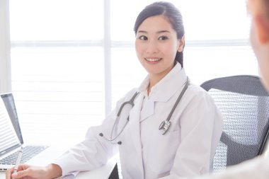 Laboratuvar önlüklü genç ve güzel Japon kadın doktorun portresi. Hastanedeki hastayla konuşuyor.