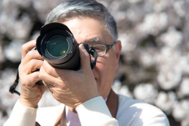 Olgun Asyalı fotoğrafçı parkta fotoğraf çekiyor.