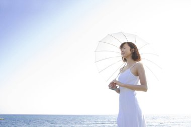 Güzel Asyalı kadın deniz kenarında şemsiyeyle poz veriyor.