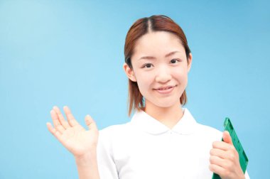 Güzel Japon hemşire portresi mavi arka planda kameraya el sallıyor.