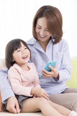 Evde cep telefonu olan Asyalı bir anne ve kız.