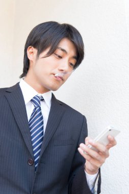 Asyalı işadamı akıllı telefon ve sigara kullanıyor 