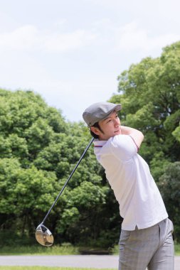 Beyaz gömlekli ve gri pantolonlu bir Asyalı golf oynuyor.