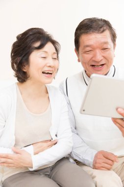 Asyalı yaşlı çift evde tablet kullanıyor. 