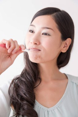 Diş fırçasıyla diş temizleyen genç Asyalı kadın.