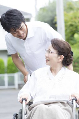 Erkek bakıcı Tekerlekli sandalyedeki Asyalı yaşlı kadına yardım ediyor