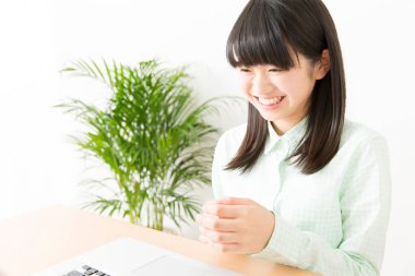 Gülümseyen Japon kız dizüstü bilgisayarla masada oturuyor.