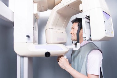 Asyalı adam gülümseyen bir makineye bakıyor, çenesinin 3 boyutlu resmini yapıyor.