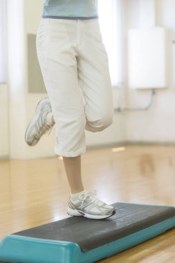 Kadın spor salonunda adım egzersizi yapıyor.