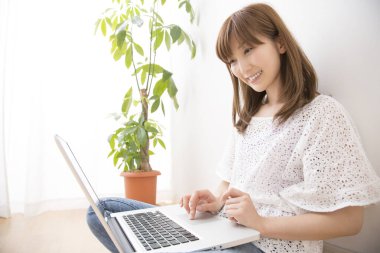 Evde dizüstü bilgisayarı olan gülümseyen güzel bir Japon kadın.