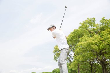Beyaz gömlekli ve gri pantolonlu bir Asyalı golf oynuyor.
