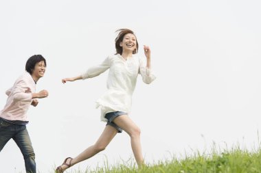 Çimenli tepede neşeyle koşan iki kişi