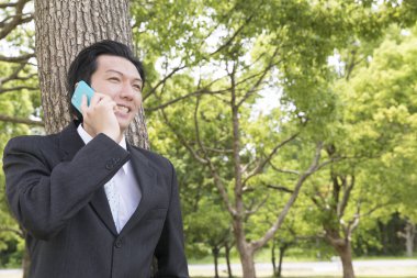 Parkta akıllı telefondan konuşan Asyalı işadamının portresi 