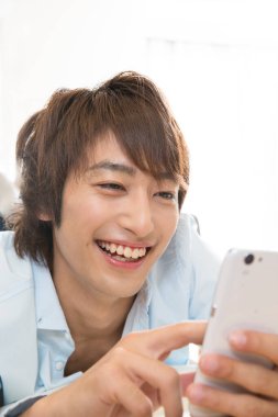 Asyalı genç adam evde akıllı telefon kullanıyor. 