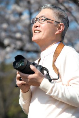 Olgun Asyalı fotoğrafçı parkta fotoğraf çekiyor.