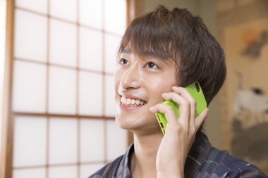 Geleneksel Yukata 'daki yakışıklı Japon genç adamın portresi. Etnik kaplıca otelinde akıllı telefon kullanıyor.