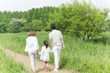 Mutlu Asyalı anne, baba ve kız parkta birlikte vakit geçiriyorlar.