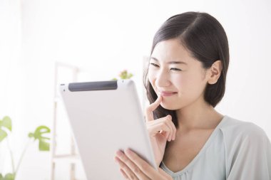 Gülümseyen Asyalı kadın oturma odasında tablet bilgisayar kullanıyor.