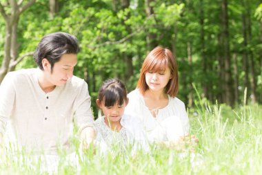 Mutlu Asyalı anne, baba ve kız parkta birlikte vakit geçiriyorlar.