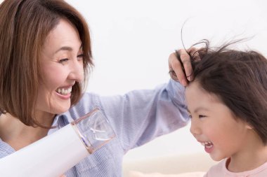 Saç kurutma makinesiyle Asyalı anne ve kızı. 