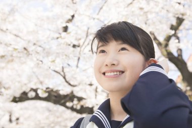 Sokakta çiçek açan kiraz ağaçlarıyla güzel Japon öğrencinin portresi.