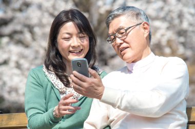 Kocasıyla birlikte parkta akıllı telefon kullanan Asyalı son sınıf öğrencisi. 