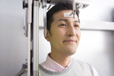 Asyalı adam gülümseyen bir makineye bakıyor, çenesinin 3 boyutlu resmini yapıyor.