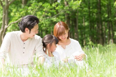 Mutlu Asyalı anne, baba ve kız parkta birlikte vakit geçiriyorlar.