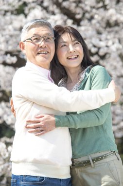 Güzel Asyalı olgun çift çiçek açan kiraz ağaçlarına karşı poz veriyor.