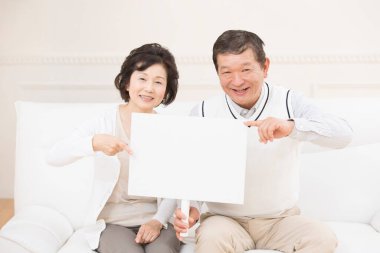 Asyalı üst düzey çift gülümsüyor ve ellerinde beyaz tahta var.