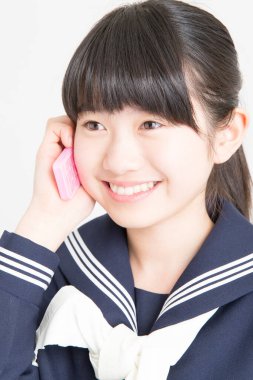 Okul üniformalı genç Asyalı kızın portresi akıllı telefondan konuşuyor.